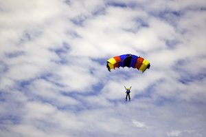 Man jumping with a colorful red, yellow and blue parachute captured against a cloudy autumn sky at an air show event.
